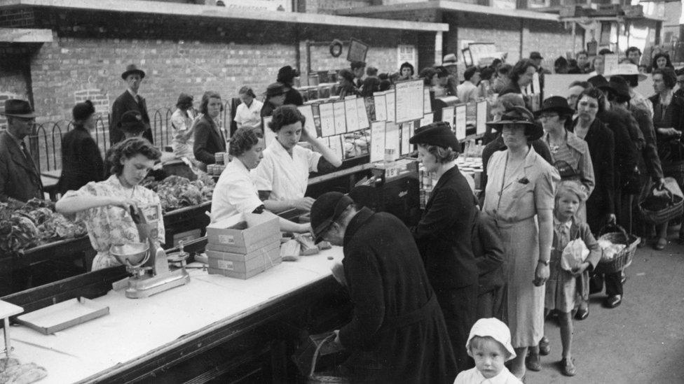 Shoppers queuing to buy food at a stall run by a department store at an open air market at Plymouth in the wake of German bombing during World War Two