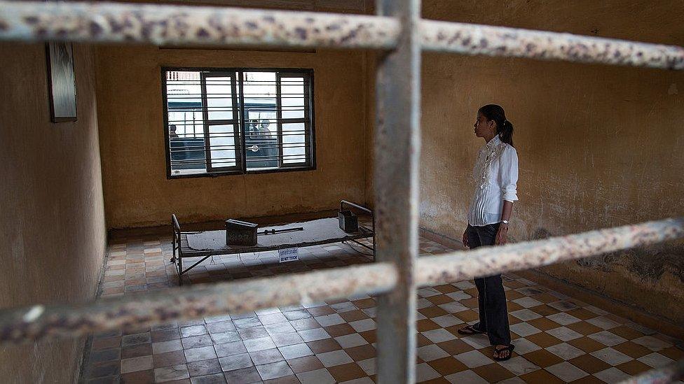 A young Cambodian woman stands in one of the torture rooms of Tuol Sleng prison