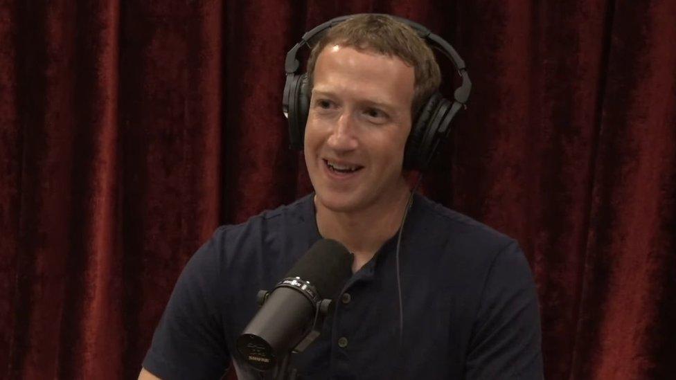 Mark Zuckerberg wears headphones and sits in front of a microphone