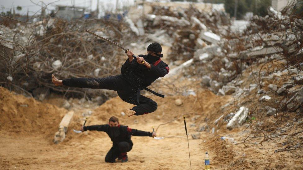 Palestinian youths demonstrate ninja-style skills in front of the ruins of buildings in Gaza, destroyed in the 2014 war