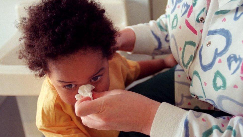 A woman wipes a child's nose