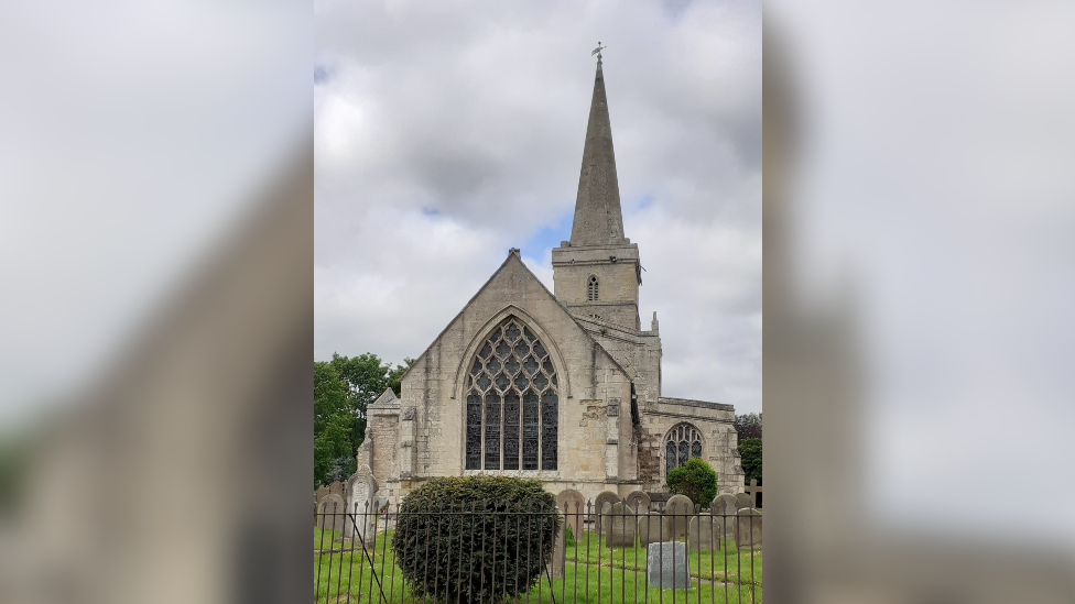 The exterior of St Wildfred's Church in Ottringham. The building is surrounded by large trees and overgrown grass.