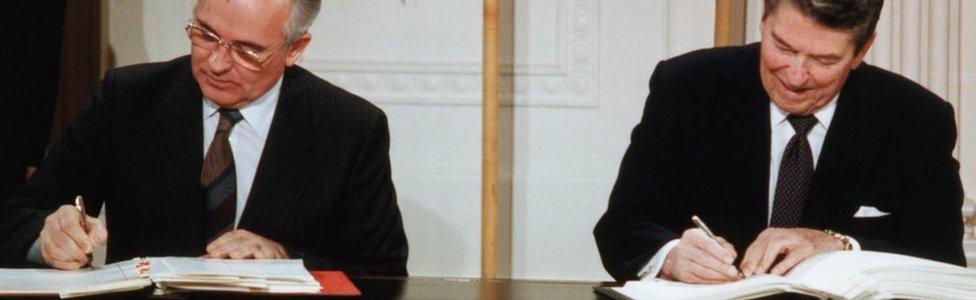 Reagan and Gorbachev Signing Arms Limitation Agreement at a table in front of their nations' flags.