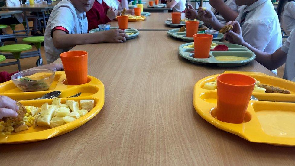 children around long table eating from trays of food