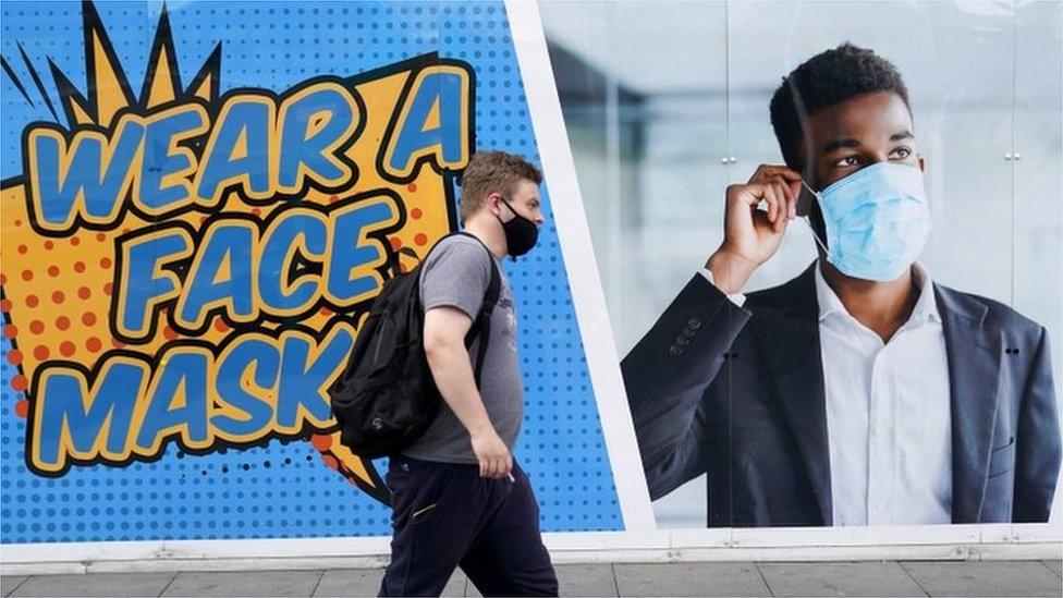 Man in mask walks past sign urging people to wear a face mask