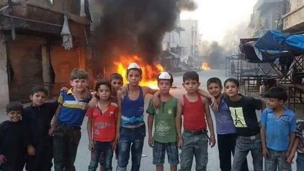 Children in Aleppo with a pile of burning tyres behind them