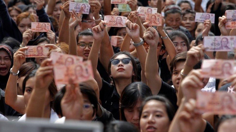 Thais hold up notes containing pictures of King Bhumibol