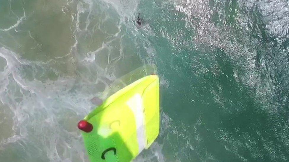 A screengrab from the drone's recorded footage shows it drop a yellow inflatable rescue device into the sea to help the struggling teenagers