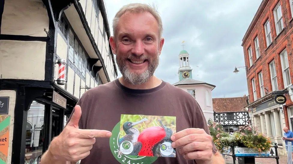 Jonny Beardmore holding a postcard