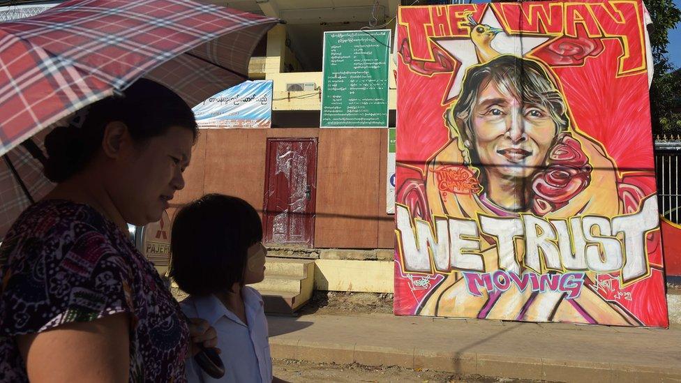 People walk past a graffiti depiction of Myanmar's opposition leader Aung San Suu Kyi outside the headquarters of the National League for Democracy party (NLD) in Yangon