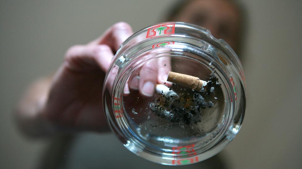 Smoker extinguishes a cigarette into a used ashtray on top of a glass coffee table