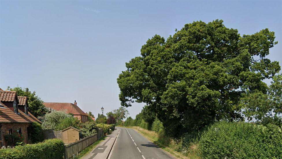 Google street view of Thurlby Road in Bassingham with a row of houses on the left hand side and a hedge and trees on the right