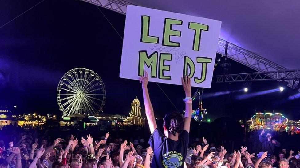 Harry Frost holding up 'let me DJ' sign in front of a crowd