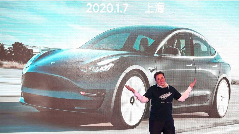 Elon Musk on stage in front of an image of a Tesla Model 3