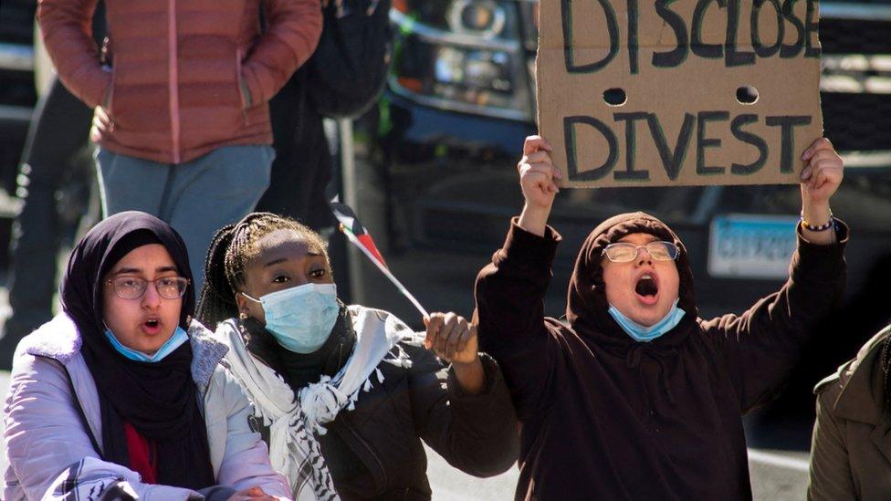 A group of three student protesters at Yale, one of whom holds up a sign saying "disclose, divest"