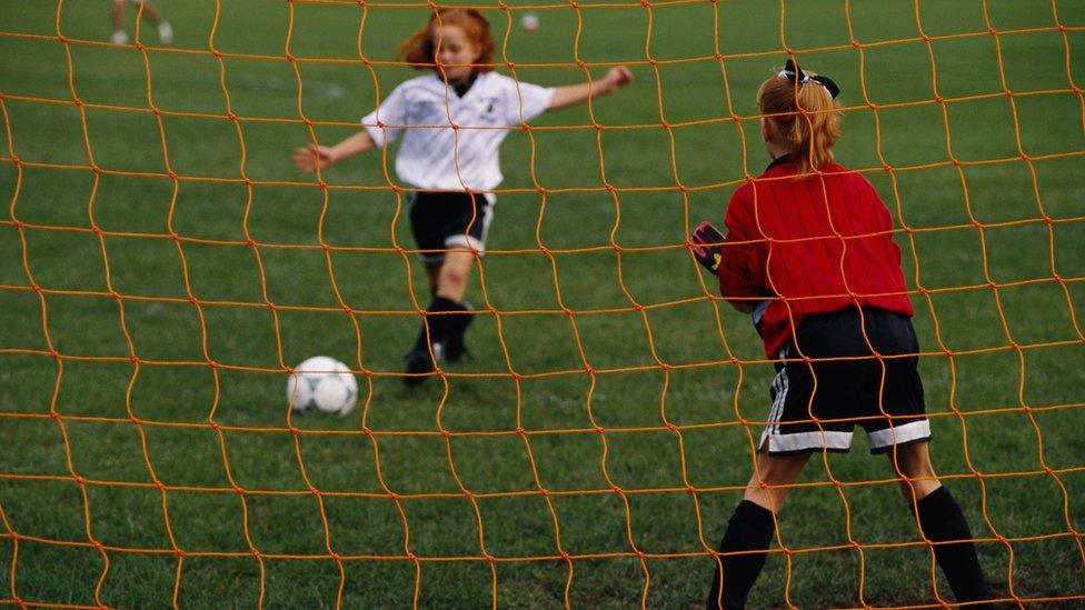 A young girl takes a shot on goal - with another girl as goalie