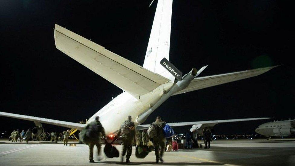 Men in army uniforms walk on tarmac towards a plane