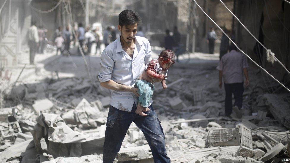 A Syrian man carries a wounded baby following a reported air strike by Syrian government forces in the rebel-held area of Douma, east of the capital Damascus, on 30 August 2015