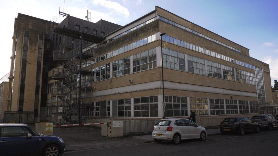 Image of the Plymouth House base in Bath. It is a beige coloured building with lots of windows and a metal staircase on the outside. Cars can be seen parked alongside the pavement