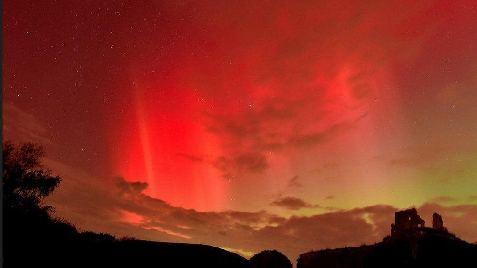 Bright red streaked sky with stars over ruins on hill in silhouette