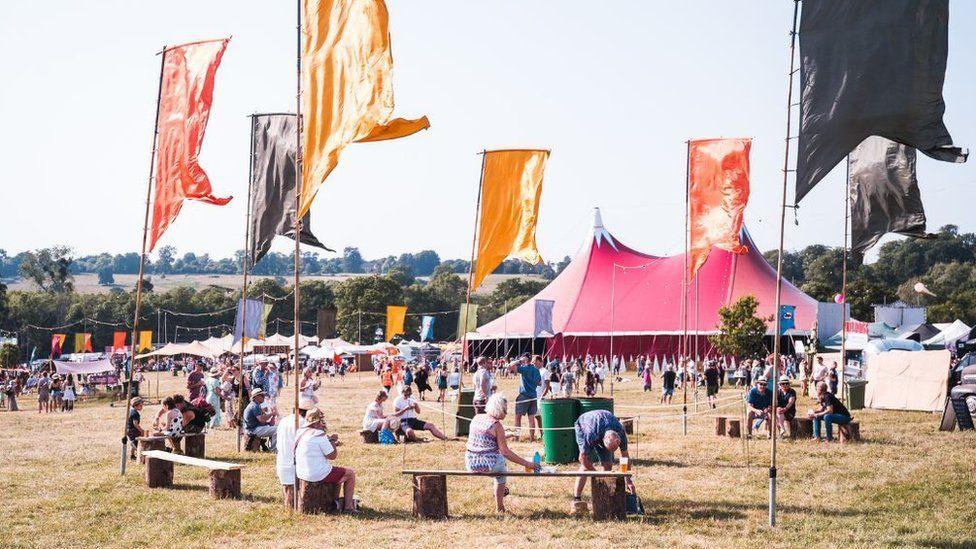 Revellers attend the Black Deer Festival in a field on a sunny day with tents in the background 