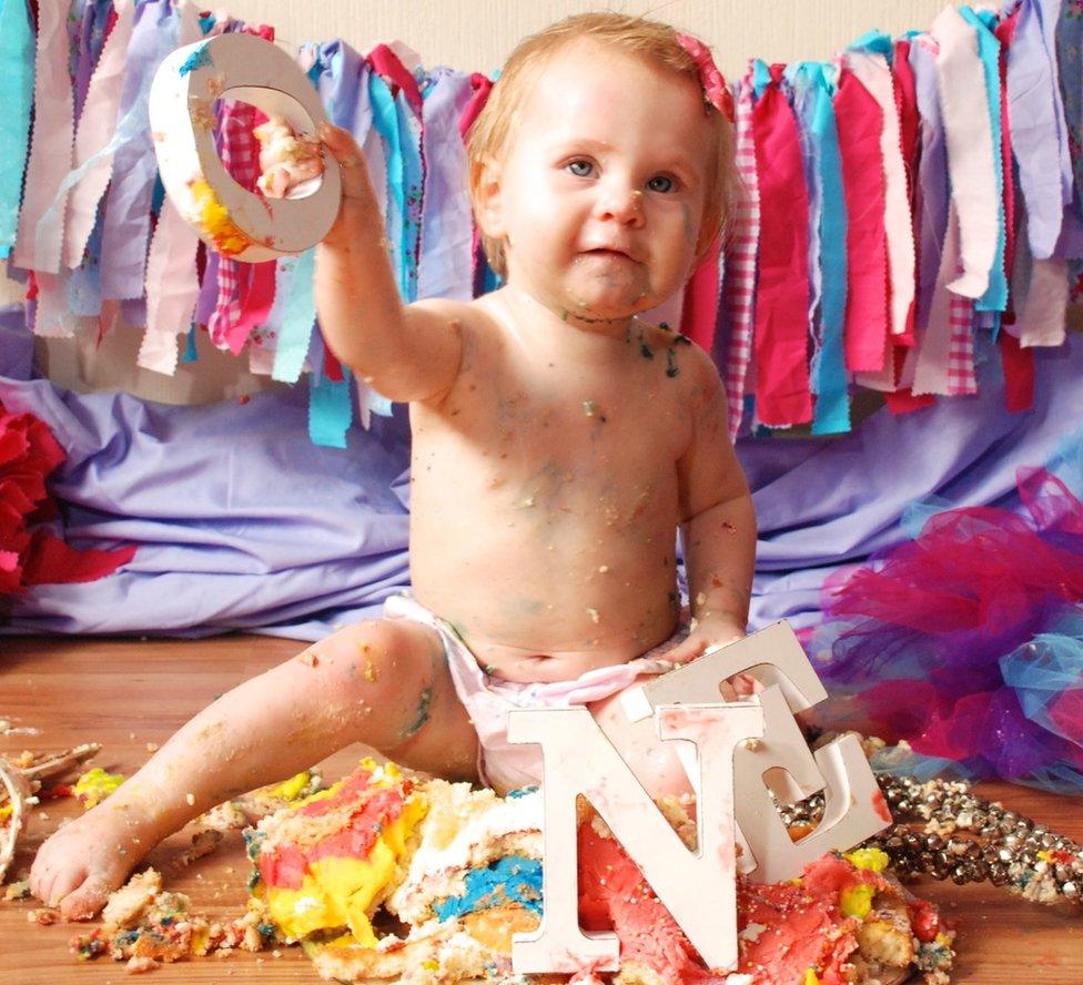 Baby Alanis holding up a letter O, from those displayed on her ONE birthday cake