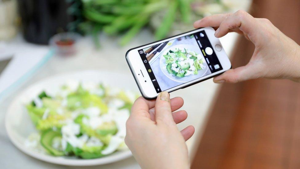 Woman with an Iphone takes picture of an avocado salad