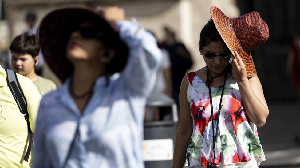 Photograph of two women shading themselves from the heat.