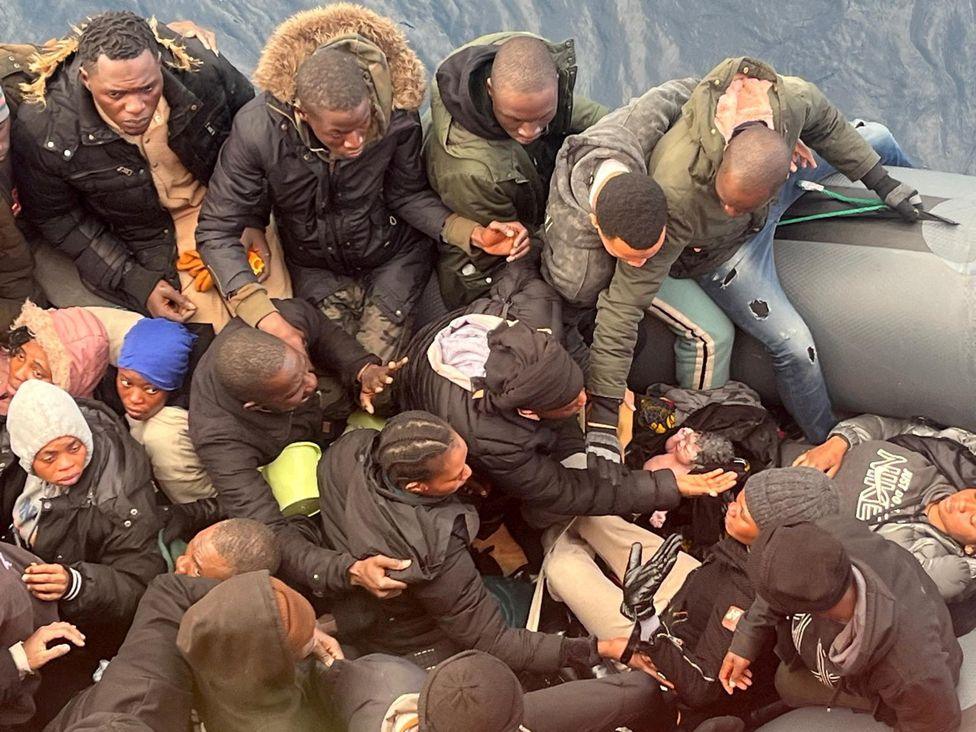 A migrant holds a newborn baby as a woman lies inside a rubber boat with other migrants who were rescued off the Canary Islands