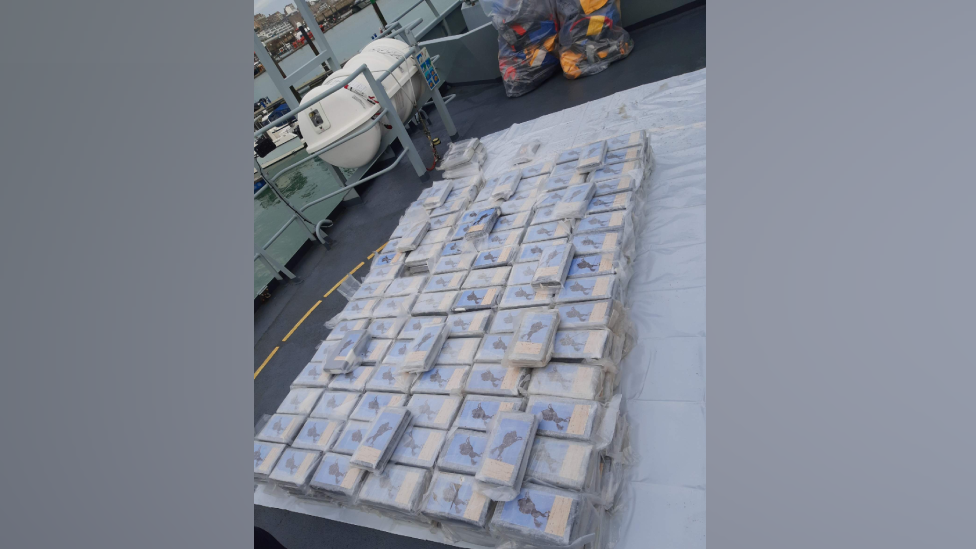 a large pile of packets of a white substance lying on a plastic sheet on what appears to be the deck of a boat or ship