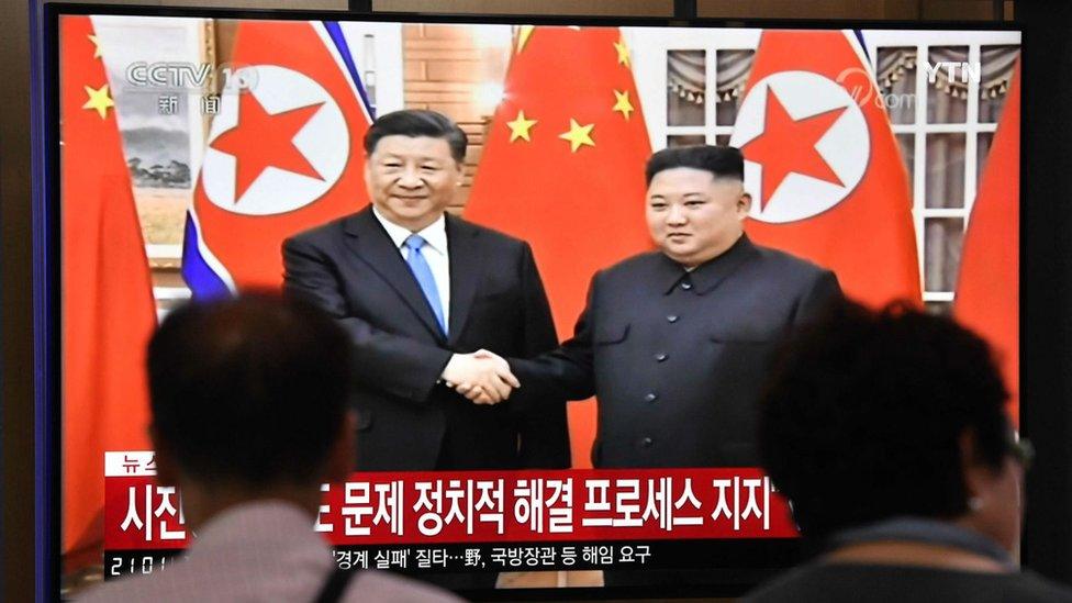 People watch a television news screen showing North Korean leader Kim Jong Un shaking hands with Chinese President Xi Jinping