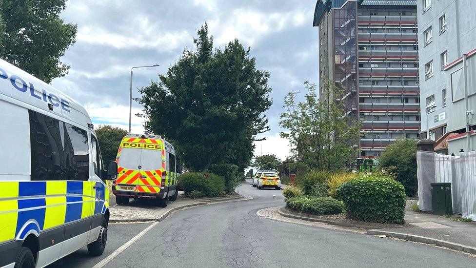 Image of three police vehicles parked on a road outside a block of flats