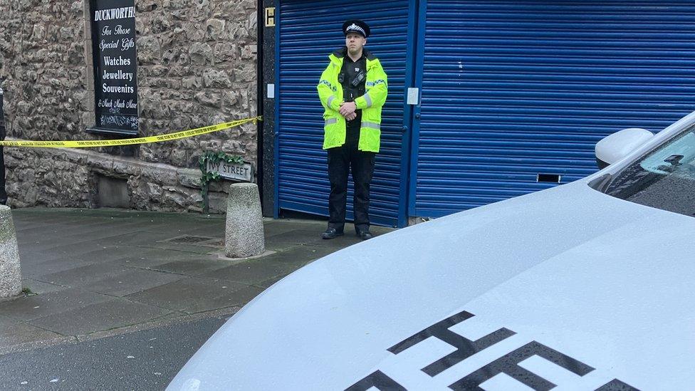 police car and a policeman beside cordoned off lane next to a pub