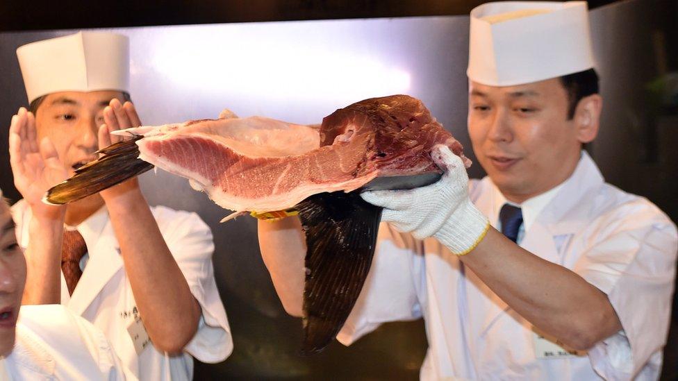 Restaurant staff hold up a cut of the tuna