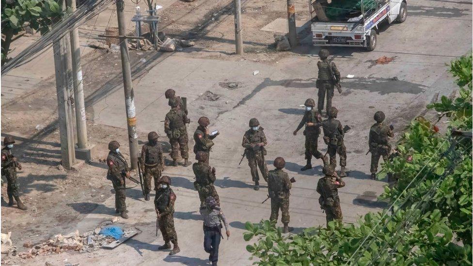 Myanmar military and riot police with weapons stand on the street during a demonstration against the military coup