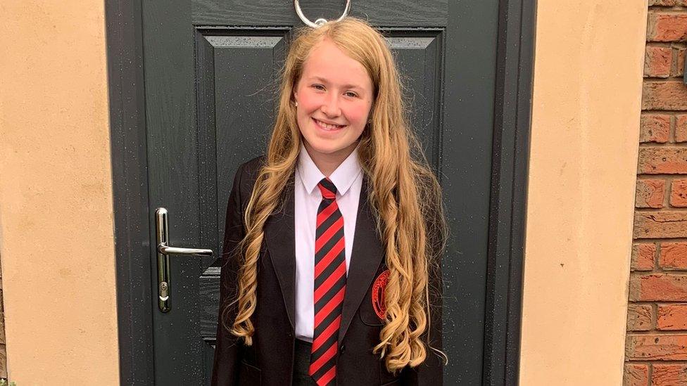 A schoolgirl standing by a front door in uniform