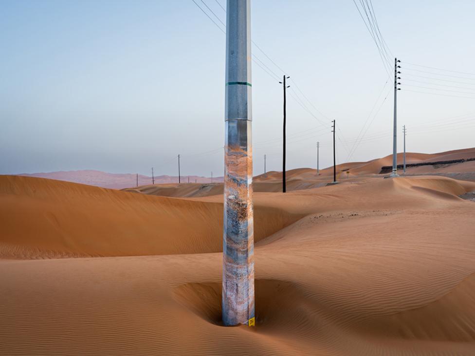 A telegraph pole stands in desert sand