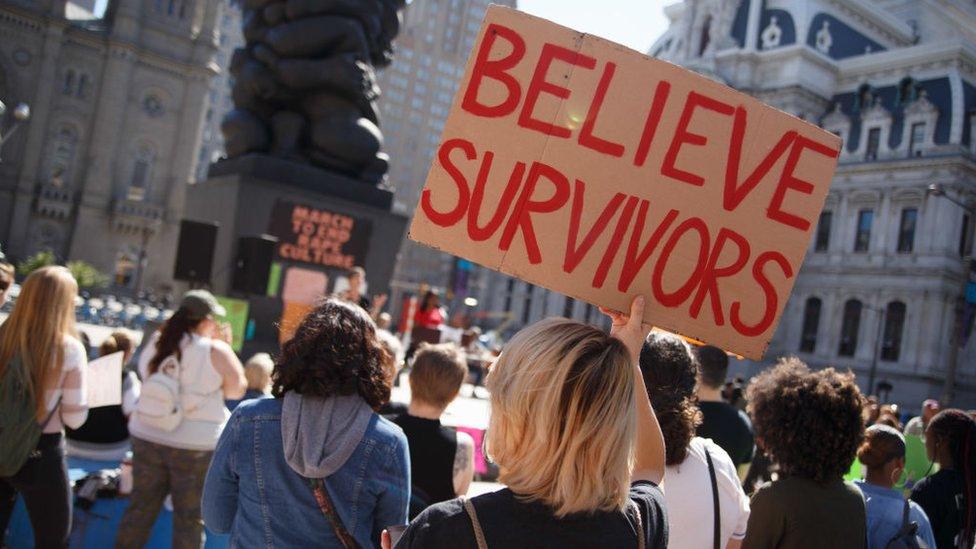 A woman holds a "Believe Survivors" sign at a rally