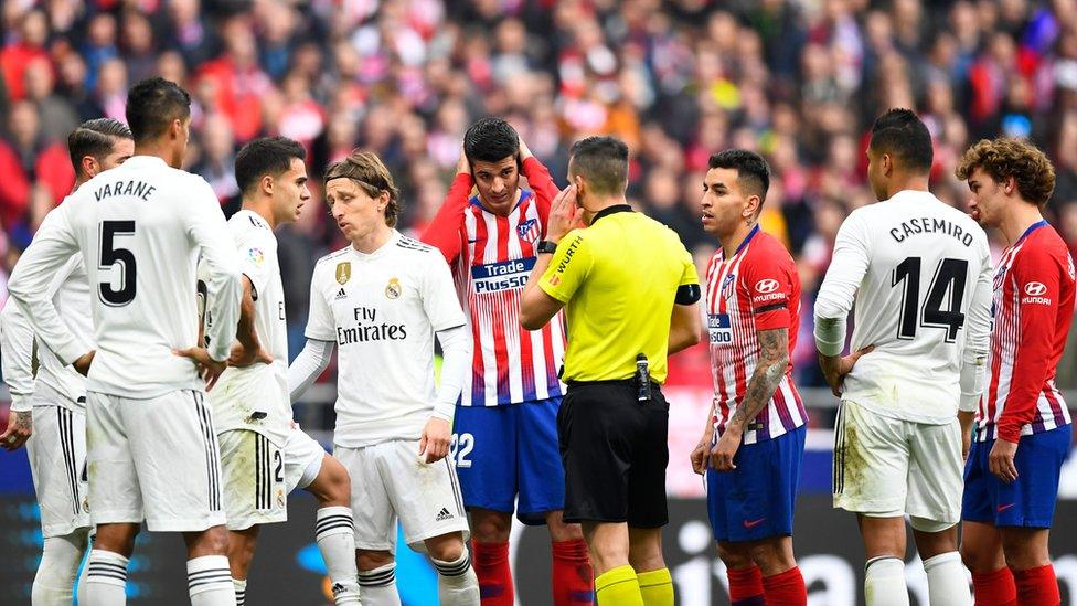 Atletico Madrid and Real Madrid players around a referr