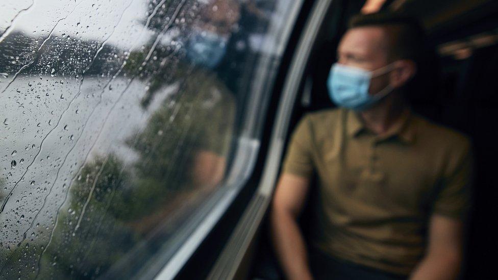 A man in a mask looking through a rainy train window