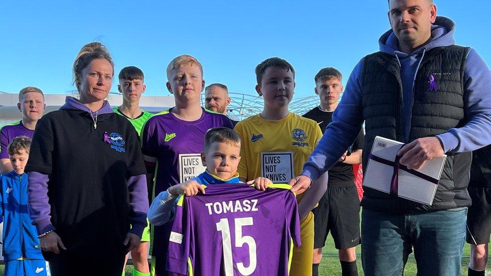 A boy and Tomasz's parents hold a shirt with the number 15 on the back