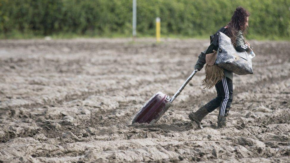 Lady walking with suitcase through mud at Glastonbury