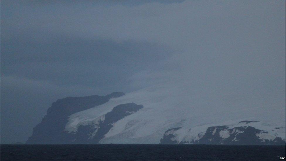 Bouvet Island in the foreground, surrounded by dark ocean waters and cloudy skies.