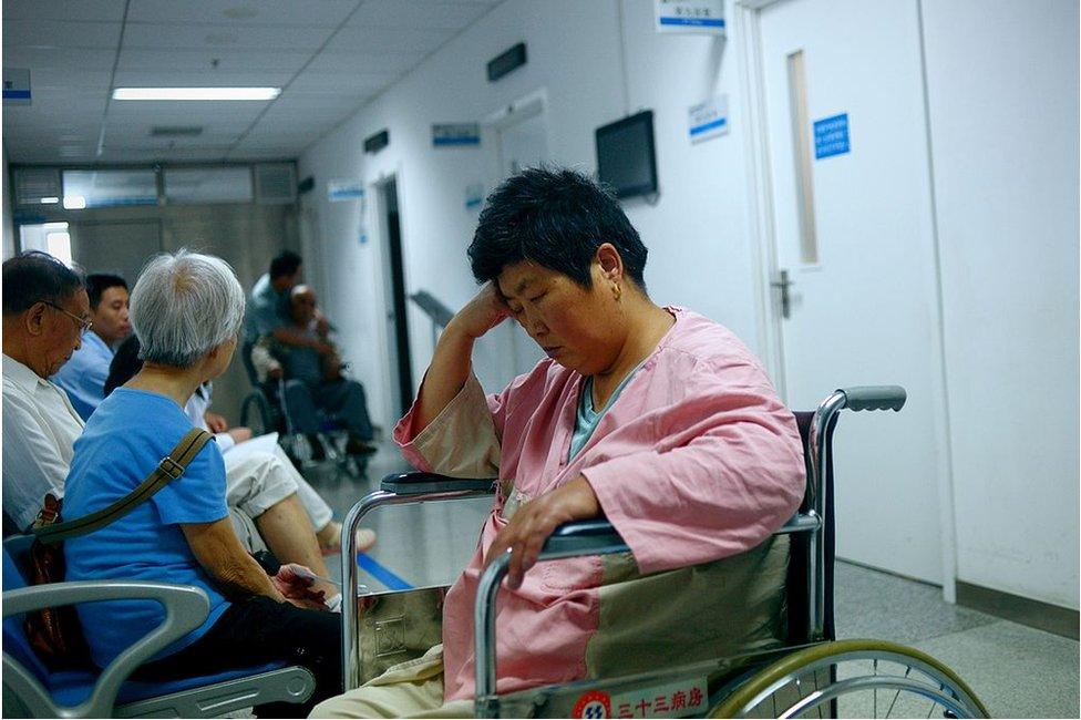 A woman (C) siting on a wheelchair waits for a health check outside a consulting room a hospital in Beijing on 3 July 2014