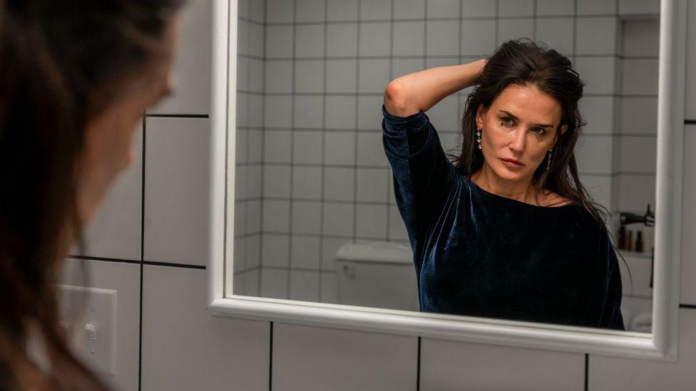 Demi Moore in The Substance, looking at her face in the mirror