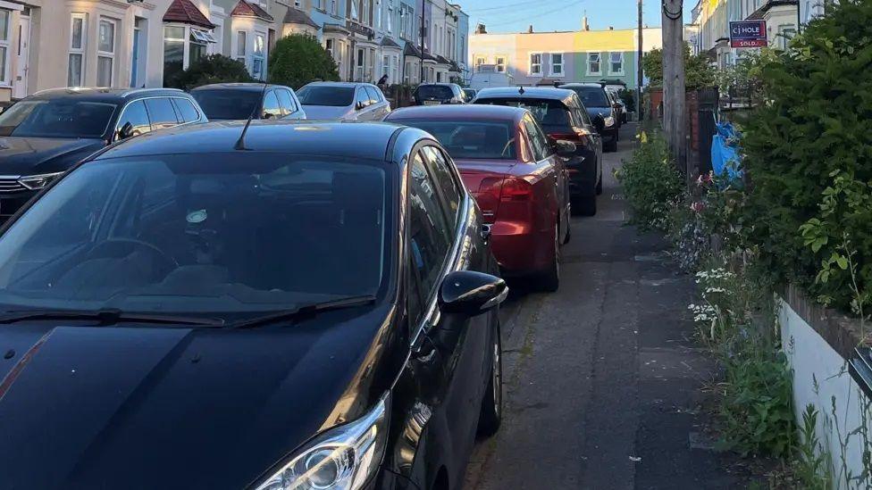 A residential street with cars parked on the pavement