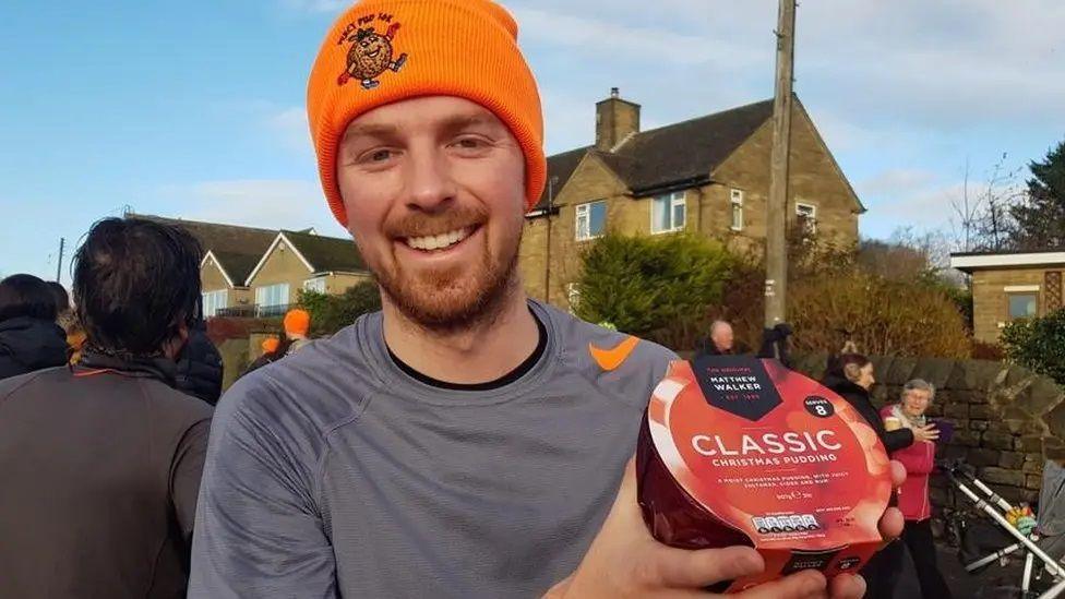 A runner in an orange beanie hat is holding a Christmas pudding.