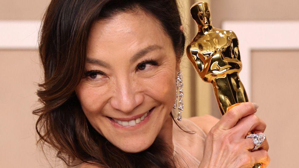 Michelle Yeoh smiling and holding her Oscar statuette up to her face after the ceremony