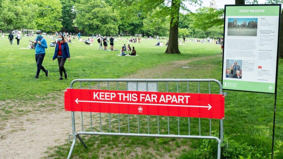 On Memorial Day weekend a sign at the entrance of Sheep Meadow in Central Park says "Keep this Far Apart" physically showing how far 6 feet is with crowds of people in side the park