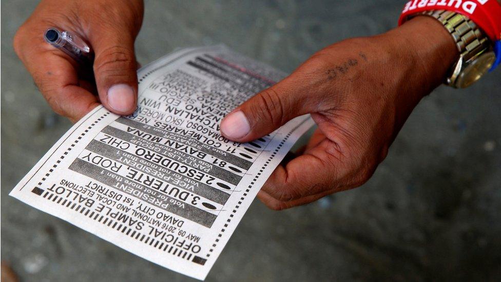 A sample ballot being held in hands belonging to a Duterte supporter, wearing Duterte wristbands, in Davao city on 9 May